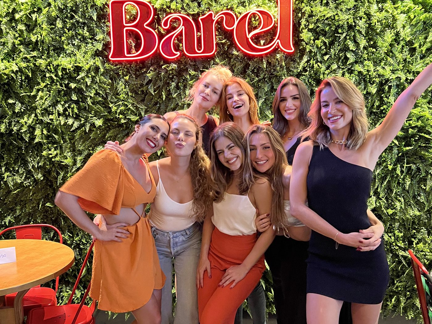 Grupo de amigas comemorando aniversário no Barel em frente à parede de plantas e ao letreiro de neon