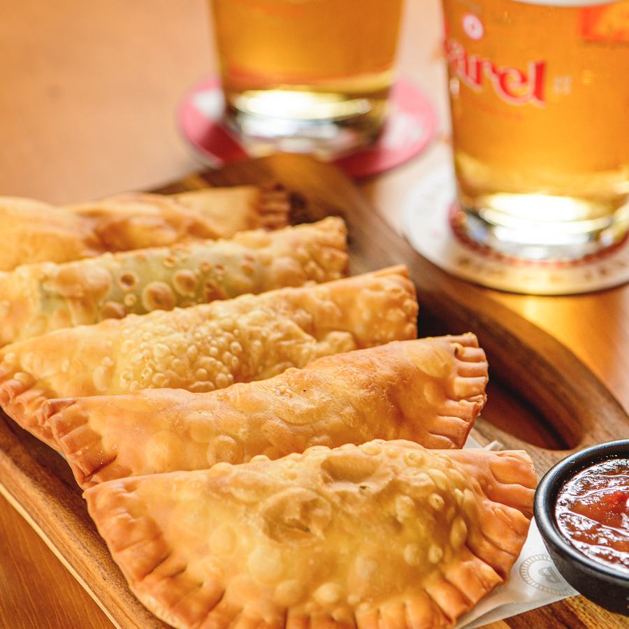 Porção de pastéis do Barel na tábua de madeira, com molho e dois chopps ao lado