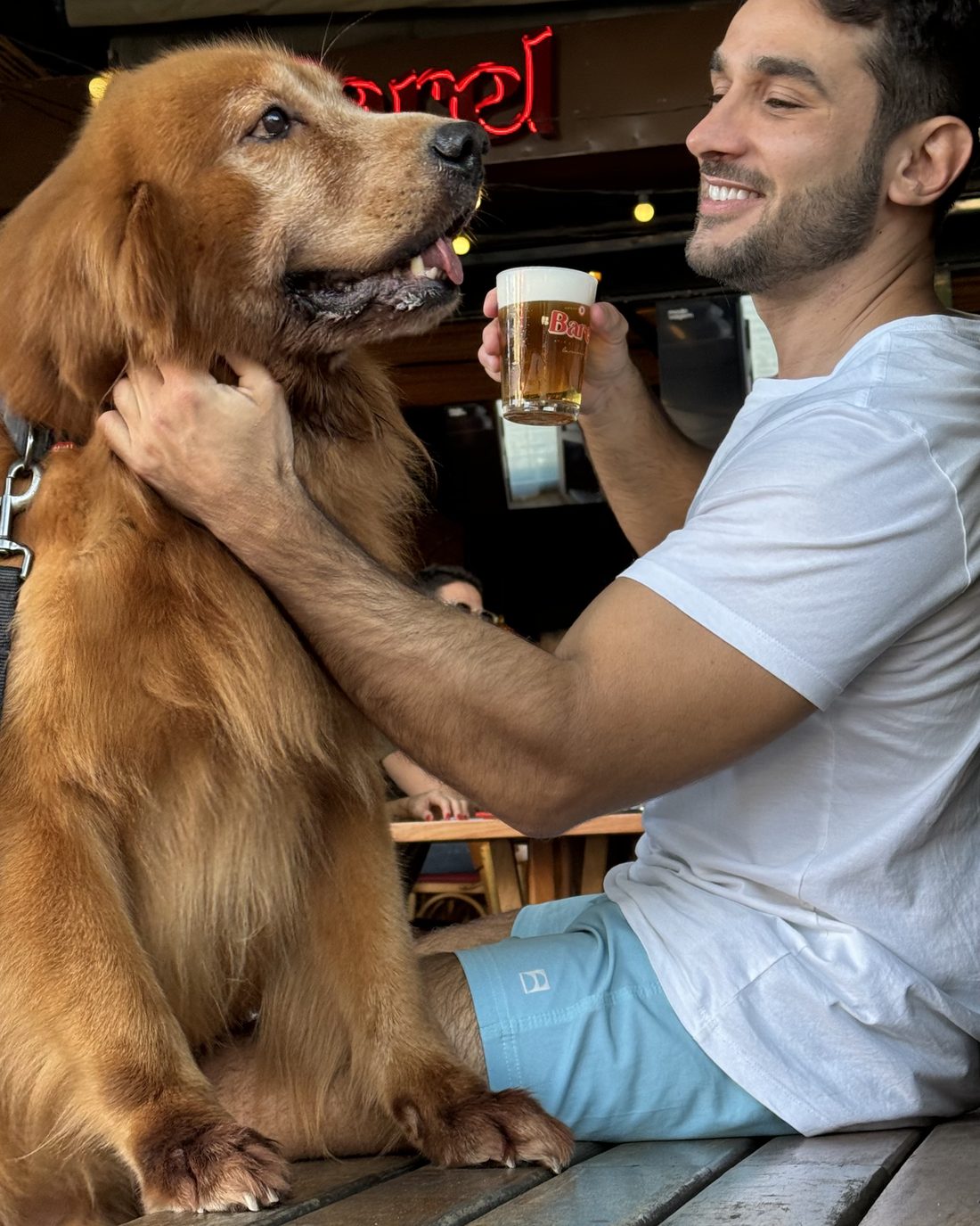 Cliente tomando chopp na calçada do Barel com o cachorro no colo, sob o letreiro vermelho
